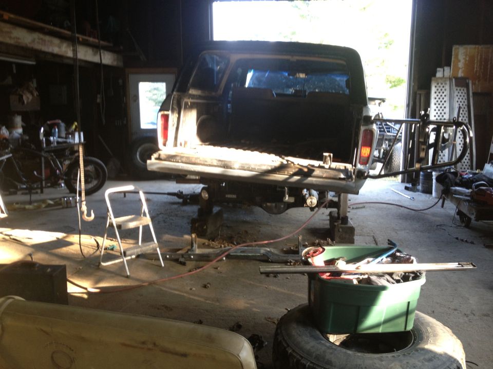 Pickup truck bed raised on jacks inside a garage, with a motorcycle and tools nearby