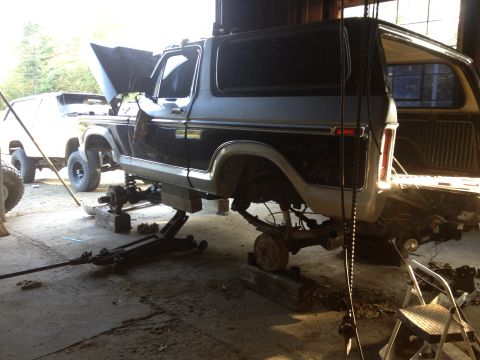 1970 Ford F-250 - A two-tone Ford Bronco is raised on jacks in a garage, with another white SUV visible in the background.