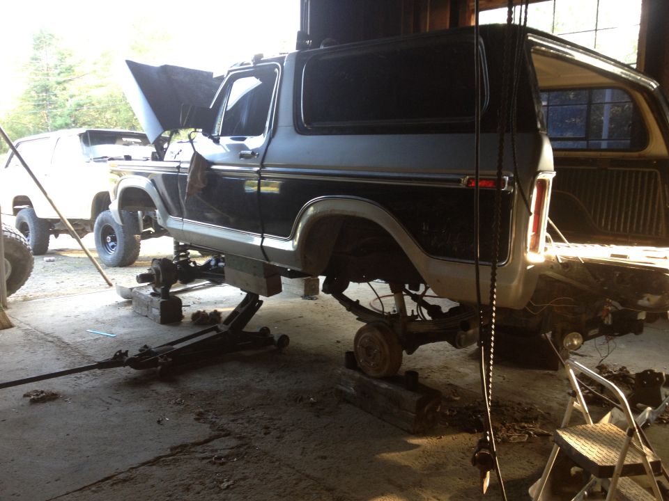 Black and gray Ford Bronco undergoing repairs, lifted on jacks with wheels removed