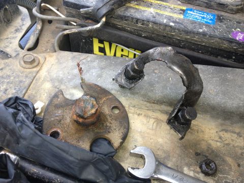 1970 Ford F-250 - Close-up of damaged automotive parts, including a bent metal bracket and a fractured mounting plate, resting on a surface near a car batter…