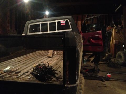 1970 Ford F-250 - The rear of a pickup truck is shown with its bed containing wiring and tools, parked inside a garage.