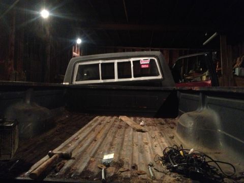 1970 Ford F-250 - The interior of a truck bed is visible, containing tools and electrical cords, with a camper shell mounted on top.