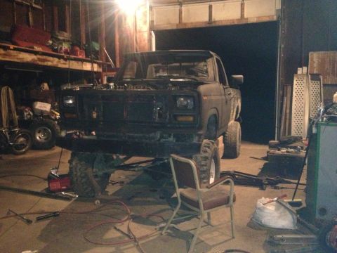 1970 Ford F-250 - A dark-colored truck is elevated on a lift inside a garage, with its hood open and various tools scattered around the floor.