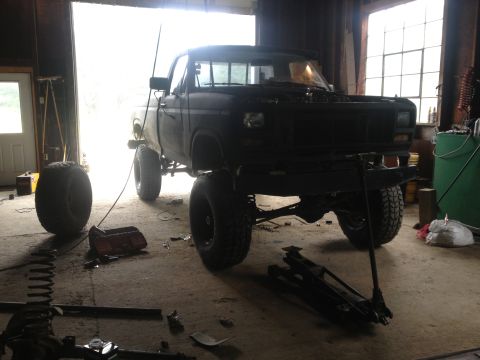 1970 Ford F-250 - A black pickup truck with a lifted suspension and large tires sits in a garage, appearing to be undergoing modifications.