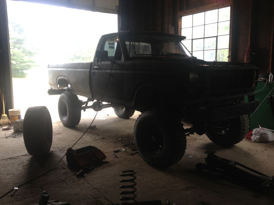 1970 Ford F-250 pickup truck with lifted suspension and large tires, parked inside a garage