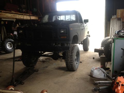 1970 Ford F-250 - This pickup truck is raised on a jack with large off-road tires, suggesting it's being worked on in a garage.