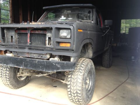 1970 Ford F-250 - Matte black Ford pickup truck, front view, grille removed, parked in a garage.