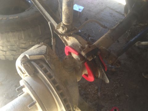 1970 Ford F-250 - Close-up of a red suspension component installed on a vehicle's axle, with a tire and brake rotor in view.