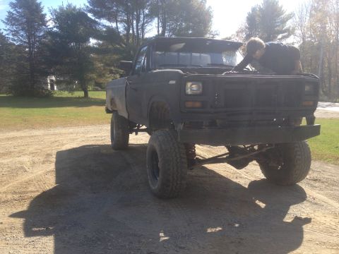 1970 Ford F-250 - A person works on the engine of a black, lifted pickup truck parked on a dirt road.