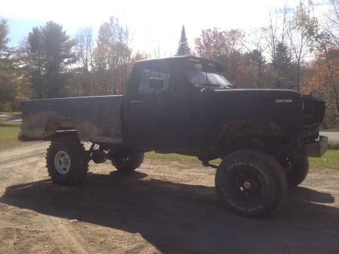 1970 Ford F-250 - A black pickup truck with a lifted suspension and off-road tires sits on a dirt road.