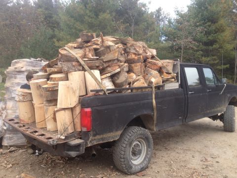 1970 Ford F-250 - A black pickup truck is heavily loaded with cut firewood, seen from the side.