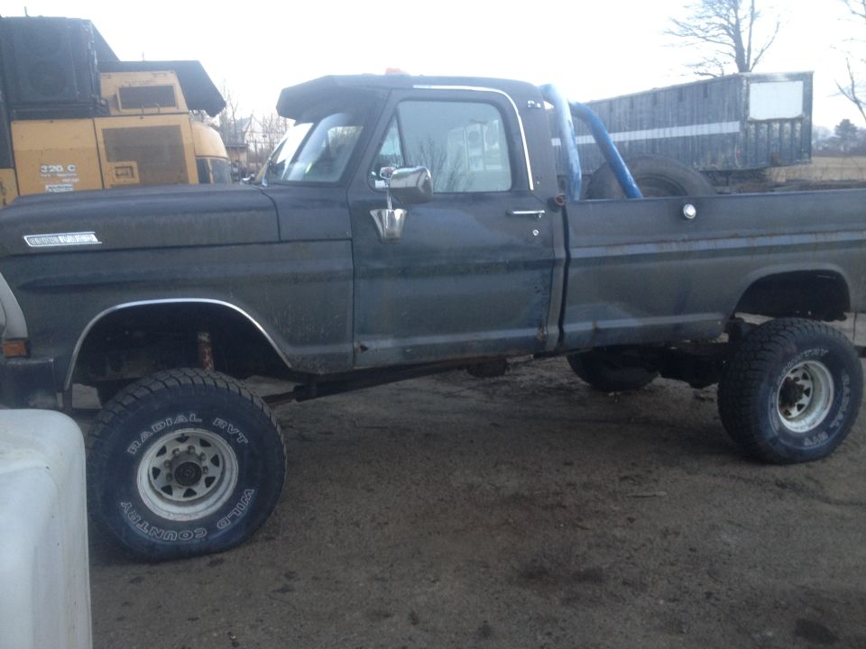 Dark green 1970 Ford F-250 pickup truck with a lifted suspension and off-road tires, seen from the side