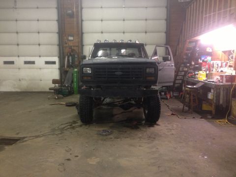 1970 Ford F-250 - A black pickup truck is parked inside a garage, showing its front end with a custom bumper and lifted suspension.
