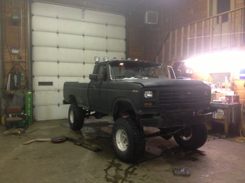 1970 Ford F-250 - This lifted pickup truck is parked inside a garage with a large overhead door.