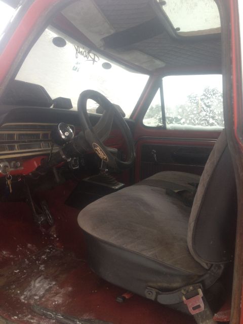 1970 Ford F-250 - The interior of a 1970 Ford F-250 shows a red dashboard, cloth seat, and a steering wheel with a Ford logo.