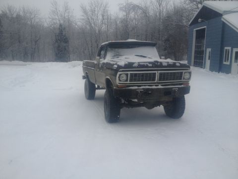 1970 Ford F-250 - A classic Ford F-250 sits in a snow-covered yard, its grille partially obscured by winter's frost.
