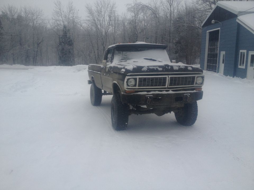 Ford F-250 pickup truck covered in snow, parked in a snowy yard next to a blue building