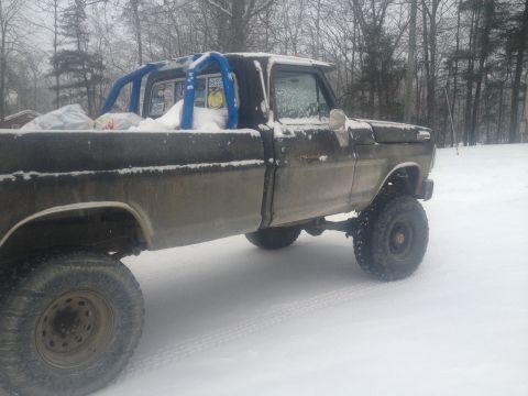 1970 Ford F-250 - A lifted Ford F-250 pickup truck sits in the snow, equipped with a blue roll cage and covered in a dusting of snow.