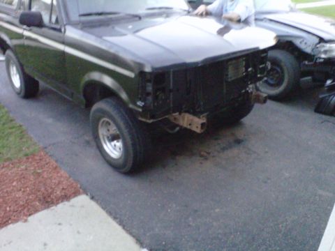 1994 Ford Bronco - Front view of a Ford Bronco, missing its bumper and grille, with another vehicle nearby.