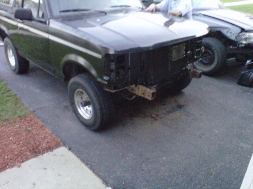 Dark green Ford Bronco with front bumper removed, parked next to another vehicle