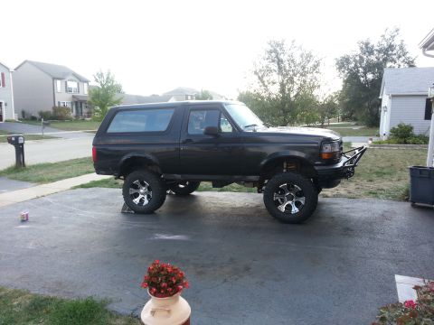 1994 Ford Bronco - This lifted black SUV is parked in a suburban driveway with houses in the background.