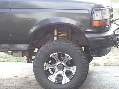 1994 Ford Bronco - A dark gray Ford Bronco is shown from the front quarter angle, highlighting its wheel and fender area.