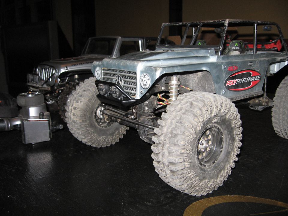 Two RC rock crawlers with large tires sit on a dark surface. One has a grille with a star emblem