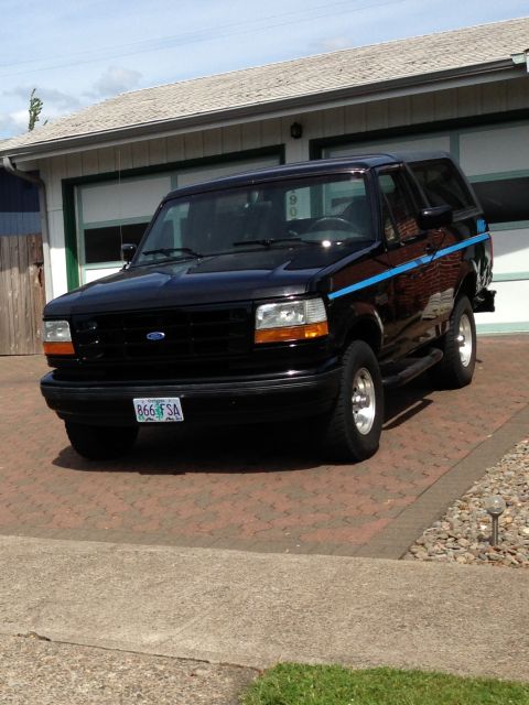 1992 Ford Bronco - A black 1992 Ford Bronco is parked in a driveway with a blue stripe on its side.
