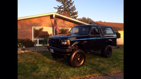 1992 Ford Bronco - This black 1992 Ford Bronco features distinctive blue pinstripes and is shown parked on a grassy lawn in front of a residential building.
