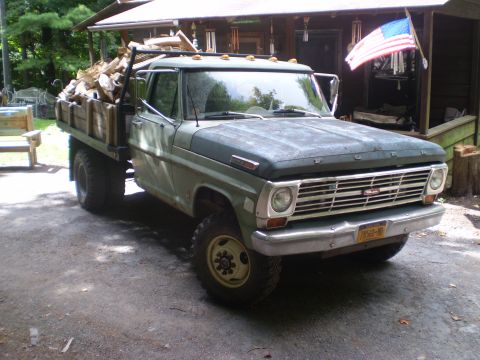 1979 Ford Bronco - 1967 Ford flatbed truck carrying a load of firewood in front of a wooden structure.