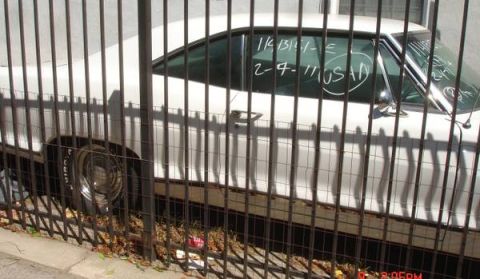 1965 Pontiac Catalina - A white 1965 Pontiac Catalina is seen from the side, partially obscured by a fence. Writing on the window indicates a date of 2-4-11.