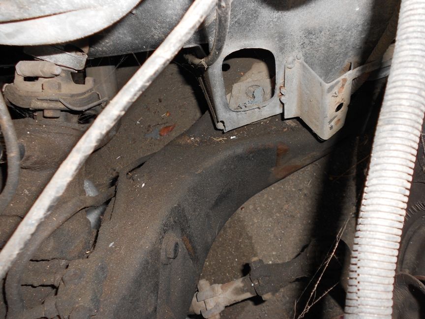 Close-up of dirty vehicle frame and suspension parts, possibly from the engine bay area