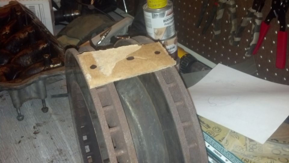 close-up of a rusty brake rotor with a piece of cardboard on top, next to a greasy engine part