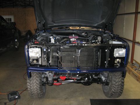 1982 Ford Bronco - Front view of a blue pickup truck with its hood open, revealing the engine compartment and grille.