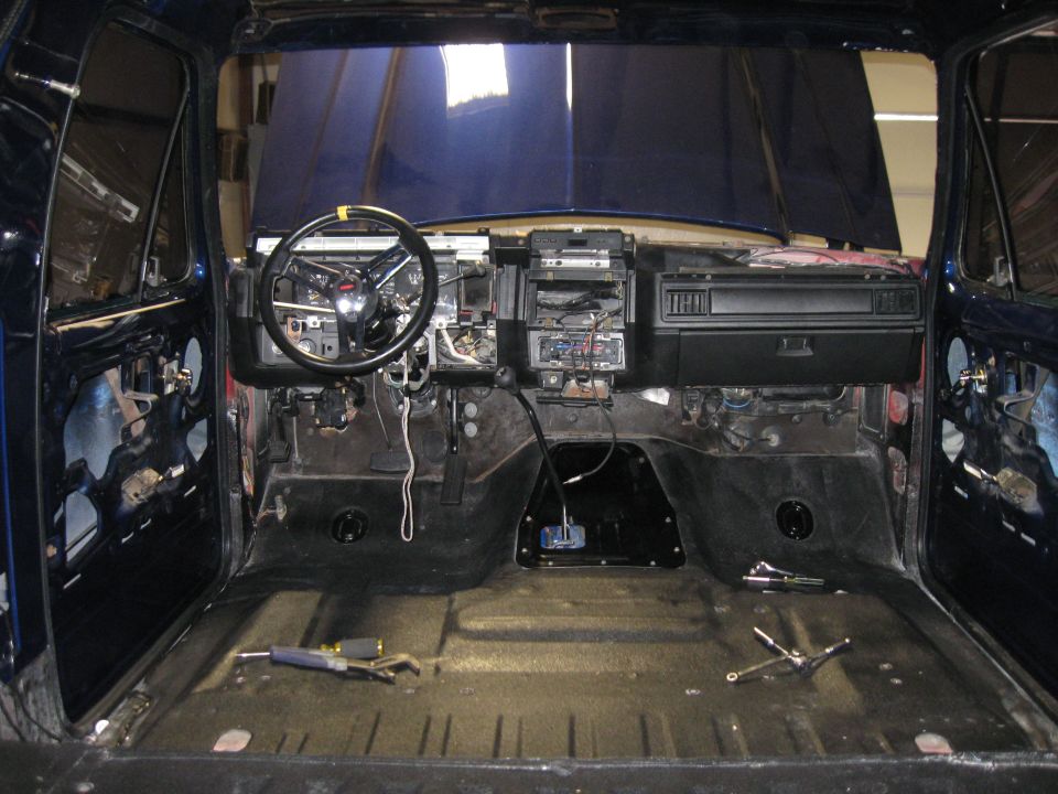 Disassembled interior of a dark blue vehicle, showing dashboard, steering wheel, and bare floor. Tools are on the floor