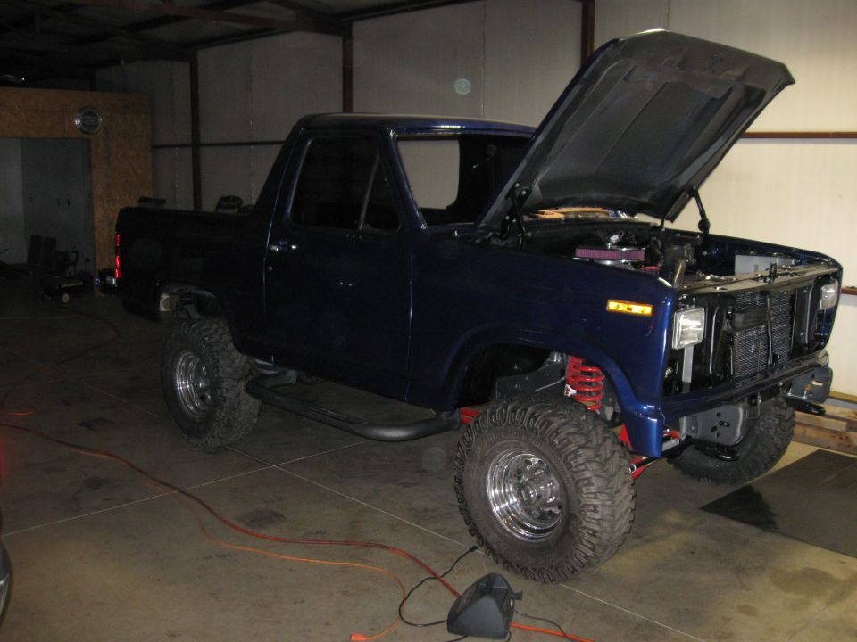 Dark blue pickup truck with hood open, lifted suspension, and large tires