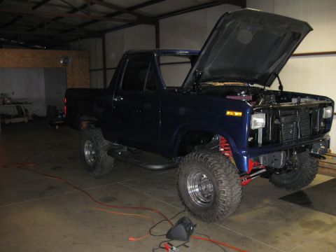 1982 Ford Bronco - This dark blue pickup truck, likely from the 1980s, is shown with its hood open and modified suspension.