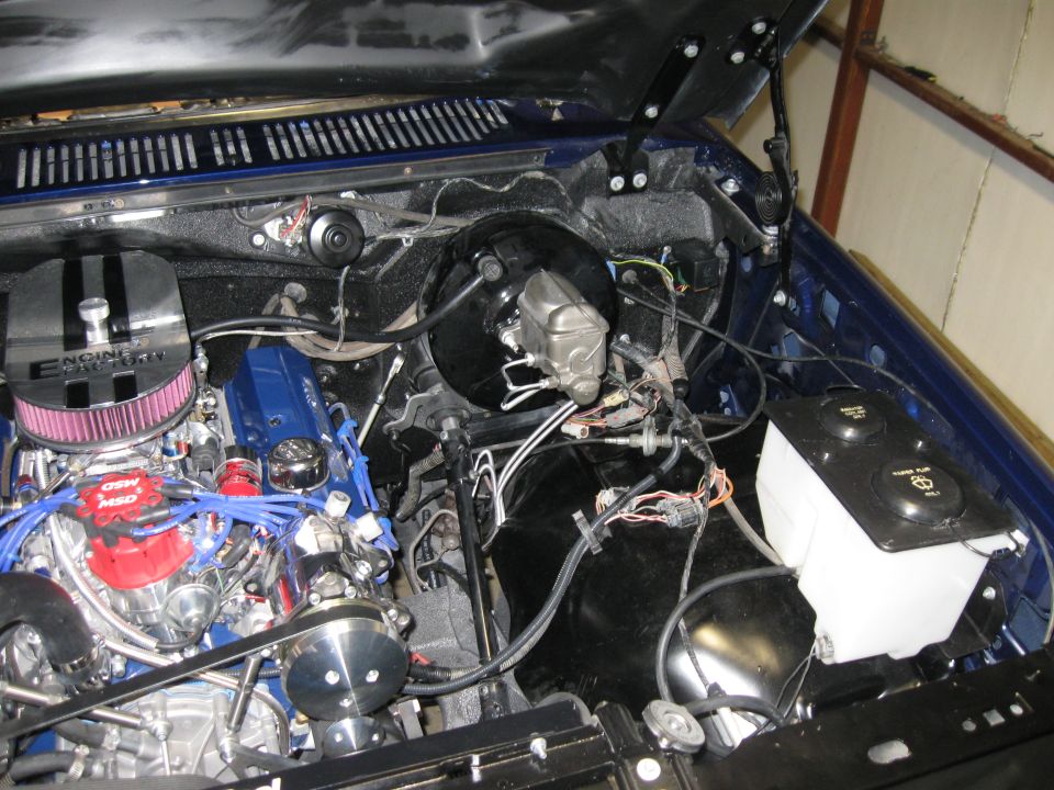 Engine bay with blue valve covers, chrome air cleaner, and red distributor cap. Brake booster and master cylinder visible