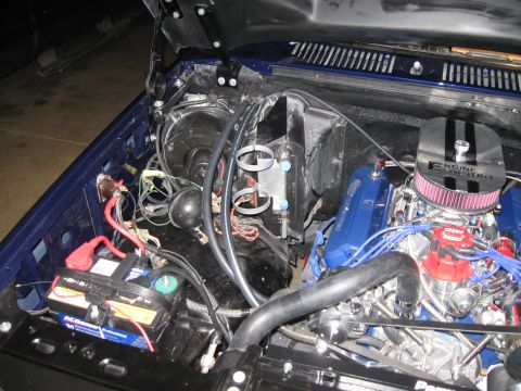 1982 Ford Bronco - The engine bay of a vehicle, showing the motor, battery, and various hoses and wires.