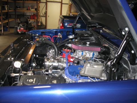 1982 Ford Bronco - The engine bay of a blue 1982 Ford Bronco, a clean setup with chrome components and an aftermarket air intake system.