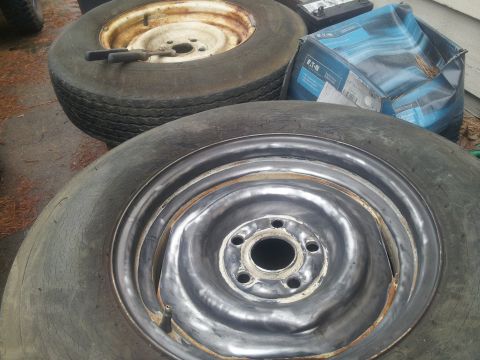 1986 Ford Bronco - A close-up view of spare tires and a car battery, with one tire showing a damaged rim.