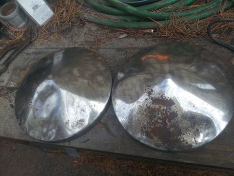 1986 Ford Bronco - Two chrome hubcaps are shown resting on a surface, with one exhibiting signs of rust.