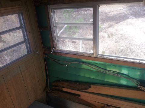1986 Ford Bronco - The interior of a camper or trailer shows wood paneling, green walls, and two windows with a view of the outdoors. Exposed wiring is visibl…