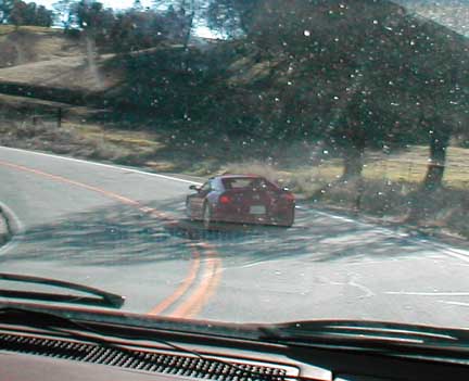 1994 Ford Crown Victoria - A red sports car navigates a curve on a two-lane road with double yellow lines.