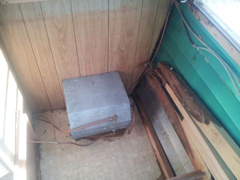 1986 Ford Bronco - The interior of a recreational vehicle shows a metal tank with plumbing, surrounded by wood paneling and exposed framing.