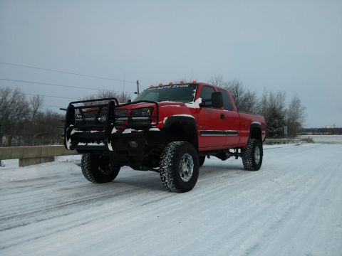 1986 Ford Bronco - A red pickup truck with a custom bull bar and lifted suspension drives on a snow-covered road.