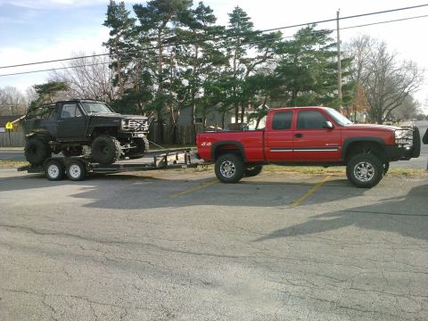 1986 Ford Bronco - A red pickup truck tows a heavily modified black SUV on a trailer.