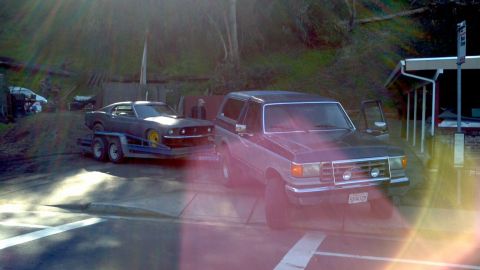 1987 Ford Bronco - A two-tone Ford Bronco is parked next to a trailer carrying a classic Ford Mustang.