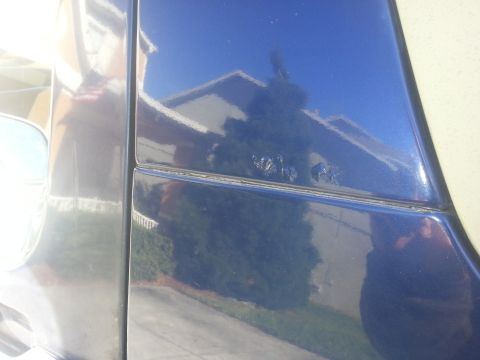 1994 Ford Bronco - Reflections of a house and trees are visible on the glossy blue paint of a vehicle's door panel.