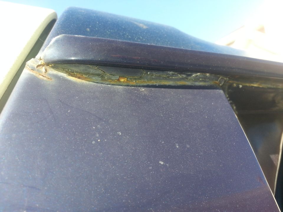 Dark blue vehicle roofline with rust around the window seal